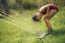 Girl Standing Under A Sprinkler In The Garden