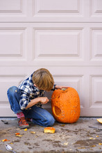 Boy Kneeling Outdoors Carving A Halloween Pumpkin