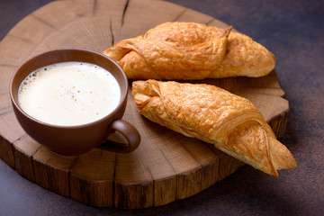 Coffee and two fresh croissants on cutting board