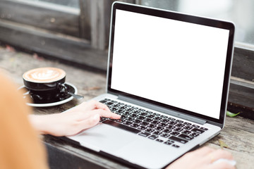 Mockup image of business woman using and typing on laptop with blank white screen and coffee cup on glass table in modern loft cafe, Soft focus on vintage wooden table.