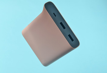 Power bank pale pink color on a blue background. External battery for gadgets. Levitation of objects.