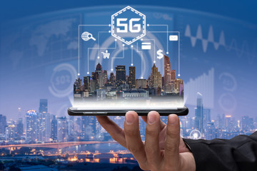 The abstract image of the business man hold the 5G hologram and cityscape is backdrop. The concept of online shopping, online payment, financial and internet of things.