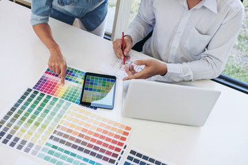 Poster - Two young interior design or graphic designer working on project of architecture drawing with work tools and color swatches, colour chart in digital tablet at workplace