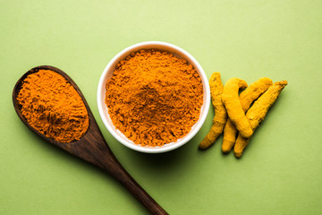 Wall Mural - Turmeric powder in ceramic bowl with raw dried turmeric over plain background

