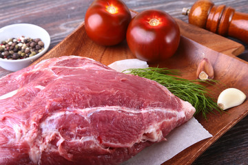 Raw pork steaks on wooden board with herbs, spices, tomatoes and pepper grinder ready for cooking. Selective focus