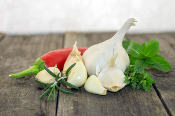 Garlic, red hot pepper and fresh spices on a rustic wooden surface with a white background