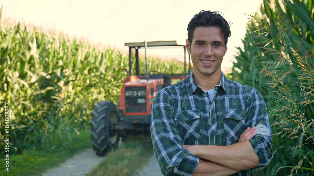 Portrait of a beautiful young farmer (student) working in the field with a tractor working in a tablet, happy, in a shirt, corn field. Concept ecology, transport, farmers, clean air, food, bio product - obrazy, fototapety, plakaty 