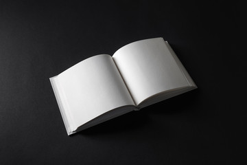 Photo of opened blank square book on black paper background.