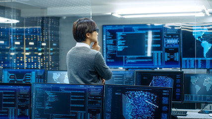 Wall Mural - In the System Control Room Technical Operator Stands and Monitors Various Activities Showing on Multiple Displays with Graphics. Administrator Monitors Work of  Artificial Intelligence.