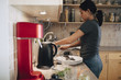 © Maskot - Side view of woman washing utensils in kitchen sink at home