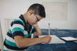 © Maskot - Side view of disabled boy writing on book while sitting at table