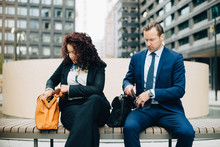Business People Sitting On Bench With Purse And Bag In City