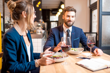 Caucasian business couple dressed strictly in the suits having discussion sitting together at the restaurant during the dinner