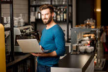 Handsome Man In Blue Sweater Working With Laptop At The Bar Of The Modern Cafe Interior