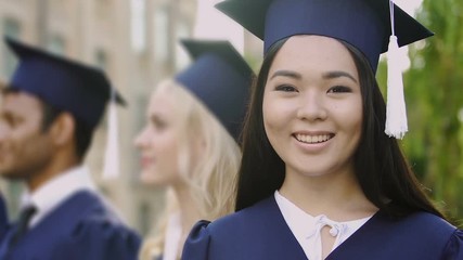 Wall Mural - Asian girl in academic dress smiling posing at camera during graduation ceremony