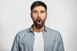 © WHstudio Leushin N - Stunned shocked young bearded male stares at camera with widely opened mouth, being surprised to see something awful or recieve bad news, poses against white background. Human attitude and reaction
