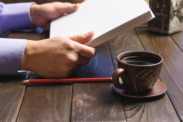 Male hand holding notepad or book with white clean pages, black coffee in brown cup, red pencil on dark wood working table, working or study concept