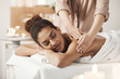 © Cookie Studio - Beautiful african girl smiling enjoying massage with closed eyes in spa salon.