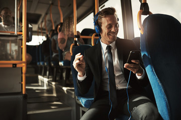 Young businessman sitting on a bus listening to music