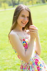 Portrait of young beautiful woman with long hair wearing flower dress in green spring park