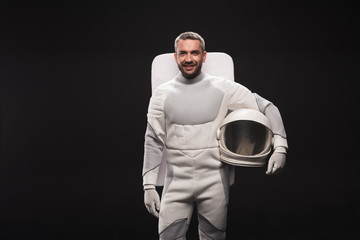 portrait of happy astronaut is holding helmet while standing in white protective suit. he is looking