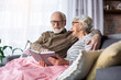 © Yakobchuk Olena - Happy moments. Portrait of serene charming husband and wife resting at living room. Man is showing woman funny picture while they are laughing and enjoying memories