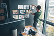 © Yakobchuk Olena - Serious bearded man ornamenting wall by different images while standing in office. Labor and design concept