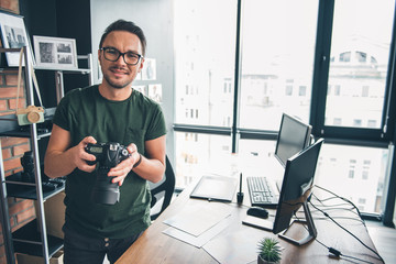 Aufkleber - Portrait of smiling young male keeping digital device in arm while locating near table in apartment. Occupation concept