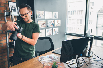 Aufkleber - Portrait of serene bearded man watching at camera while holding it in hand. He stand near desk in office. Work concept