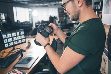 Aufkleber - Outgoing unshaven photographer holding camera and looking at it in room. Job concept