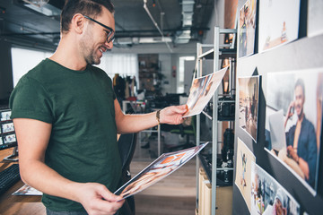 Aufkleber - Side view smiling unshaven photographer looking at pictures while standing in apartment. Job concept