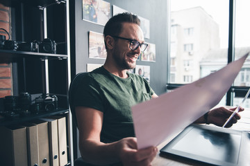 Aufkleber - Side view outgoing unshaven man watching at photos while sitting at desk in office. Occupation concept