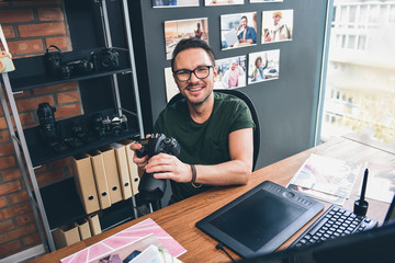 Aufkleber - Portrait of beaming unshaven man keeping appliance for taking photos while sitting at table in room. Occupation concept