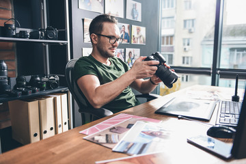 Aufkleber - Side view smiling unshaven man keeping camera in hand while situating at desk in room. Occupation concept