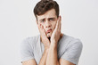 Shocked stunned emotional man keeps hands on cheeks, being troubled to listen advices of his parents isolated against blank studio wall background. European male can`t believe in shocking news