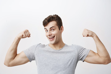 Wall Mural - Positive emotional man smiles, shows muscles on his arms, feels proud to be strong and have strength, says: I am hero. Muscular male athlete raises arms with joy, shows how strong he is.