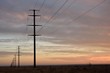 Long row of electricity pylons and power lines fading into the distant horizon at sunset in a rural setting