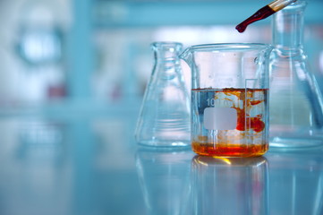 Wall Mural - clear glass beaker with orange drop solution in science laboratory background