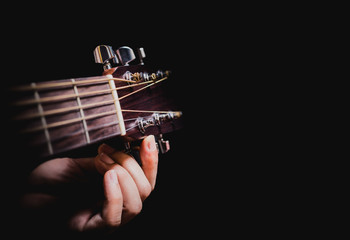 Wall Mural - closeup male musician hands tuning acoustic guitar strings, isolated on black