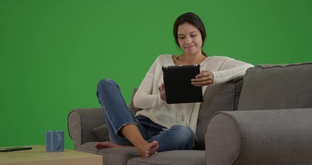 Wall Mural - Wide shot of attractive Caucasian girl browsing the internet on her tablet with greenscreen studio wall. Millennial White girl her tablet on Chroma key.