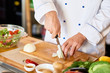 Close up of unrecognizable cook cutting onions and other vegetables with chef knife while working in modern kitchen, copy space