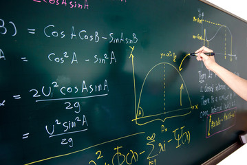 Closeup of hand writing complicated math equation on black board.