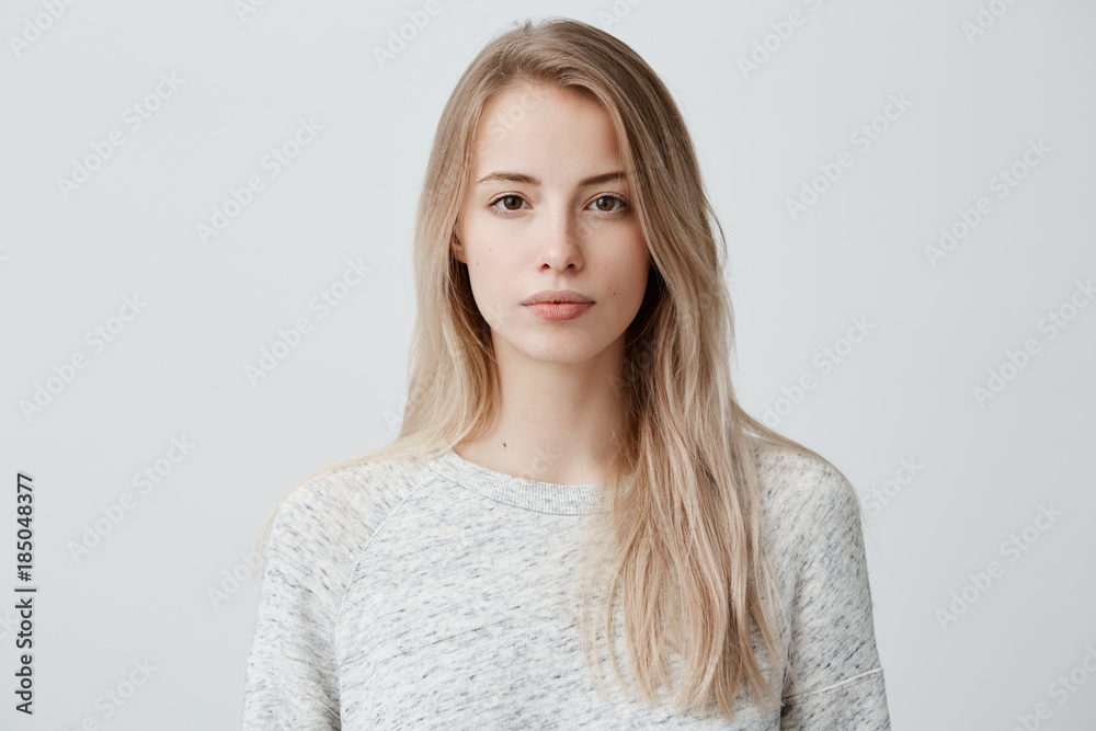 Confident good-looking beautiful woman with blonde dyed hair with healthy pure skin dressed in casual clothes looking seriously at camera. Youth and beauty concept - obrazy, fototapety, plakaty 