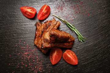 Wall Mural - Tasty grilled ribs with slices of fresh tomato on dark background