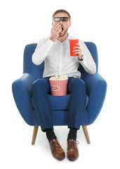 Young man with 3d glasses and drink eating popcorn while sitting in armchair during cinema show on white background