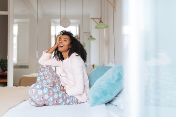 Happy beautiful young black woman relaxed sitting in the bed .