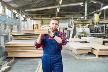 Wall Mural - Portrait of handsome young factory worker looking at camera while carrying long wooden board moving material in workshop, copy space