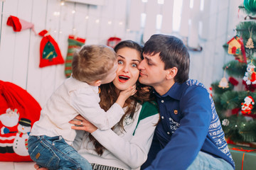 New Year's picture of happy family on background of Christmas decorations. Smiling mother and father with their son sitting and having fun