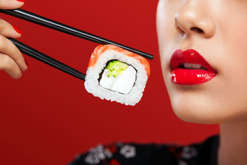 Closeup portrait of Asian woman with sushi eating sushi and rolls on a red background. Black Friday sushi sale.