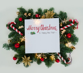 Creative Christmas layout made of christmas winter decoration and evergreen tree twigs and glowing lights, flat lay New Year scene with Merry Christmas greeting